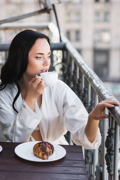 Bella donna bruna in vestaglia bianca bere caffè e distogliere lo sguardo — Foto stock