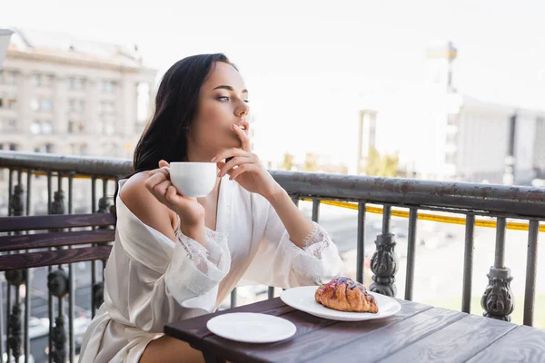 Femme brune en robe blanche buvant du café et tenant les doigts près de la bouche — Photo de stock