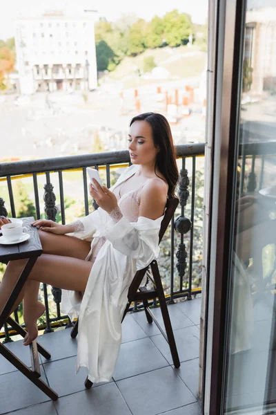 Brunette woman sitting on balcony and holding smartphone — Stock Photo