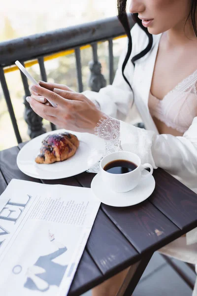 Vista recortada de la mujer desayunando en el balcón y mensajes de texto en el teléfono inteligente - foto de stock