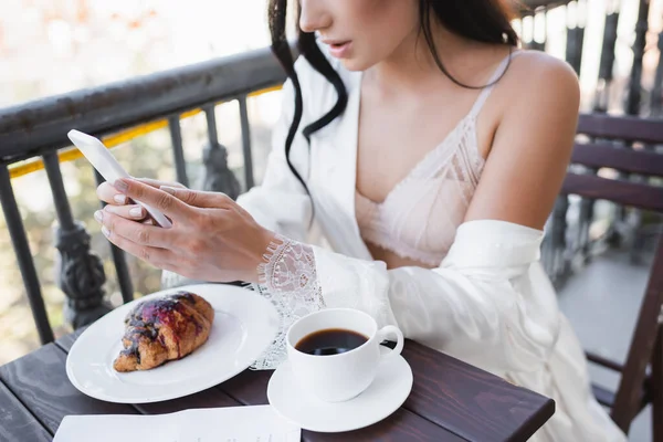 Частичный вид женщины, завтракающей на балконе и переписывающейся на смартфоне — стоковое фото