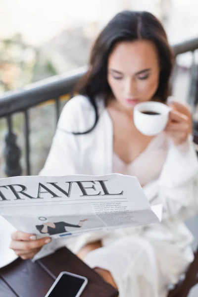 Donna bruna in vestaglia bianca seduta sul balcone e leggendo il giornale — Foto stock