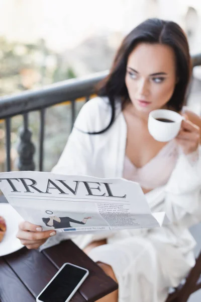 Brunette woman in white robe sitting on balcony and reading newspaper — Stock Photo