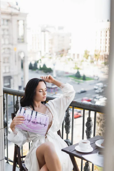 Donna bruna in vestaglia bianca seduta sul balcone e rivista di lettura — Foto stock