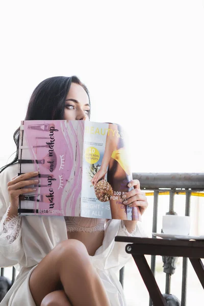 Donna bruna in vestaglia bianca seduta sul balcone e rivista di lettura — Foto stock
