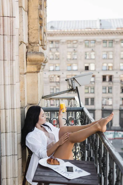 Mulher de camisa branca bebendo suco de laranja na varanda — Fotografia de Stock