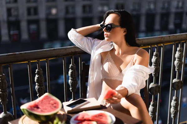 Brünette Frau in beiger Unterwäsche und weißem Hemd isst Wassermelone auf Balkon — Stockfoto