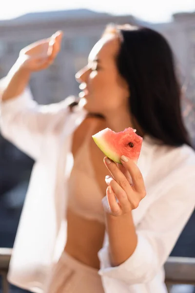 Morena comiendo sandía en el balcón y cubriendo la cara con la palma - foto de stock