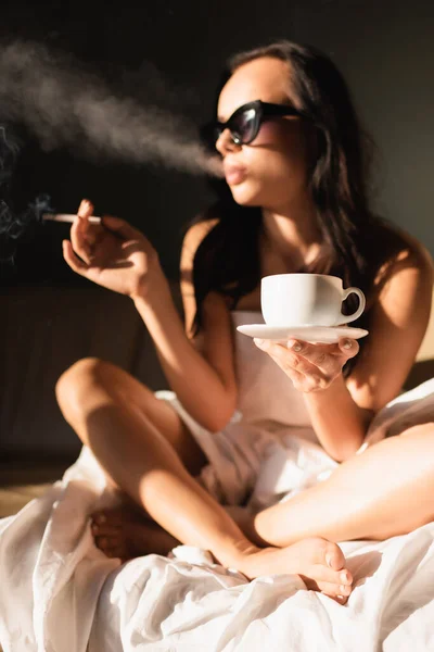 Sexy brunette woman covered in white sheet smoking cigarette and drinking coffee — Stock Photo