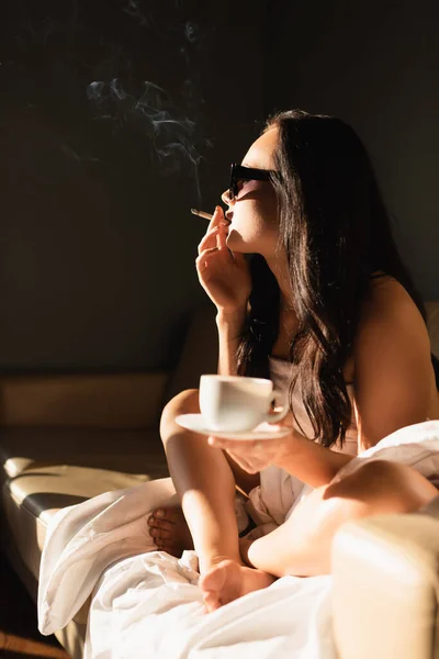 Sexy morena mujer cubierto en blanco hoja fumar cigarrillo y beber café - foto de stock