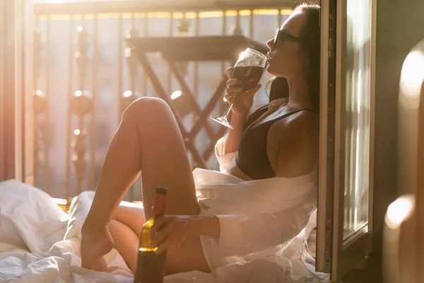 Brunette femme en lunettes de soleil et chemise blanche boire du vin sur le balcon — Photo de stock