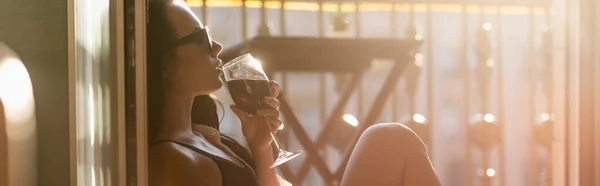 Brünette Frau mit Sonnenbrille trinkt Wein auf Balkon, horizontales Banner — Stockfoto