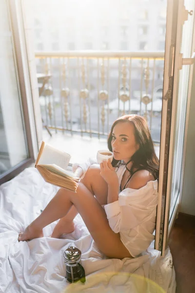 Красивая брюнетка женщина читает книги и пить чай сидя на одеяле — стоковое фото