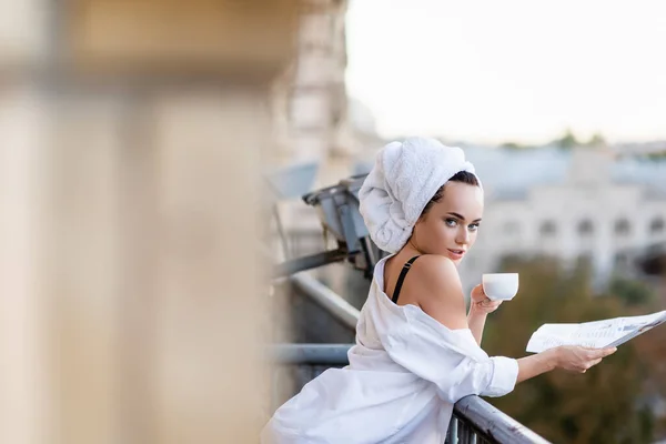 Sexy jeune femme en chemise blanche avec serviette sur la tête tenant journal et boire du thé sur le balcon — Photo de stock