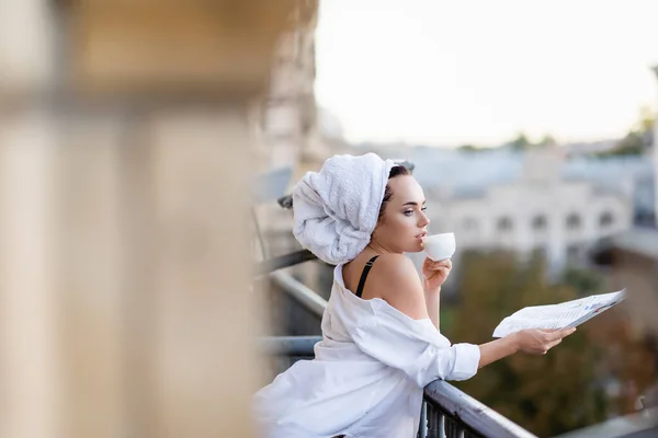 Sexy giovane donna in camicia bianca con asciugamano sulla testa che tiene giornale e beve tè sul balcone — Foto stock