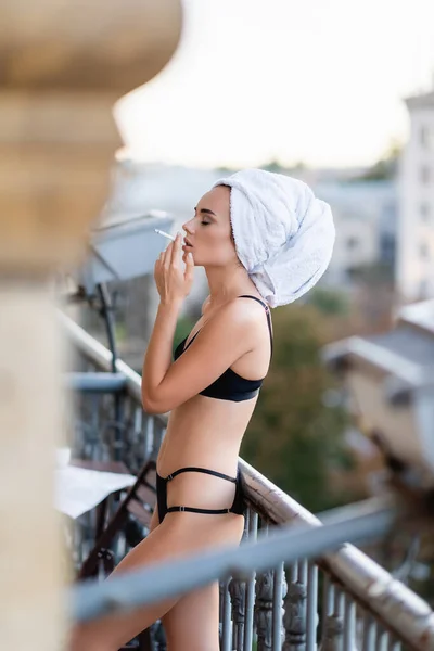 Sexy jeune femme en sous-vêtements noirs avec serviette sur la tête cigarette fumeur sur le balcon — Photo de stock