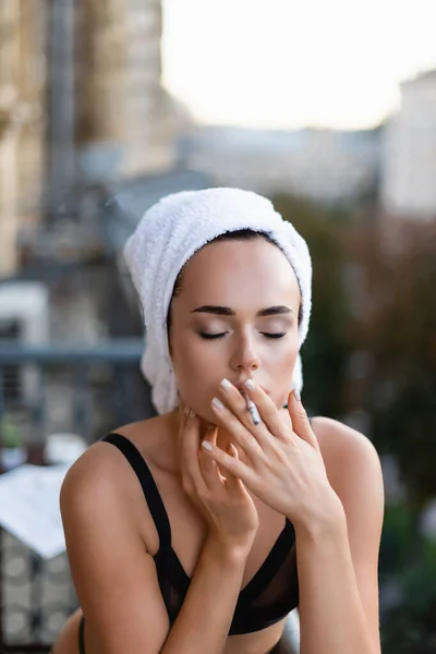 Сексуальная молодая женщина в черном белье с полотенцем на голове, курящая сигарету на балконе — стоковое фото