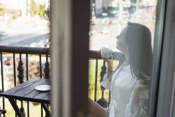 Brunette woman with closed eyes drinking tea and sitting on balcony — Stock Photo