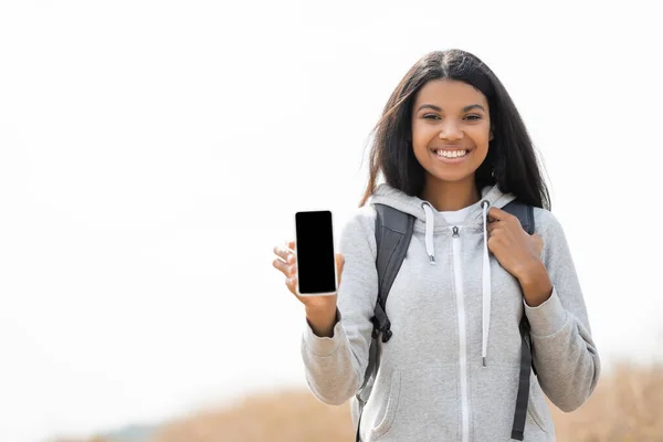 Sorrindo afro-americano caminhante mostrando smartphone ao ar livre — Fotografia de Stock