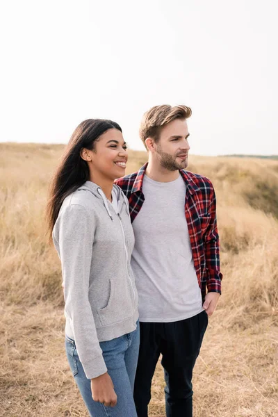 Sonriente mujer afroamericana de pie cerca de novio en el césped al aire libre - foto de stock