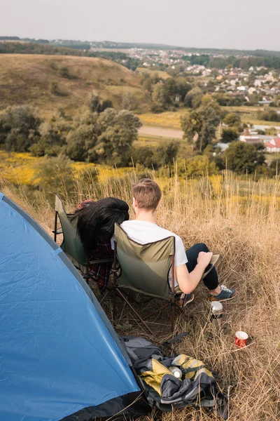 Visão traseira de turistas sentados perto de mochilas e tenda no gramado — Fotografia de Stock