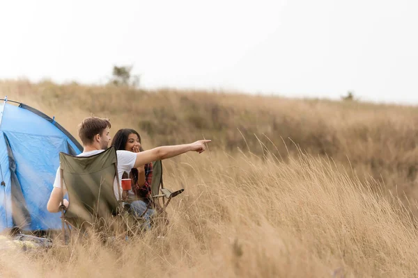 Мужчина указывает пальцем на африканскую американку с чашкой на стуле и палаткой на газоне — стоковое фото