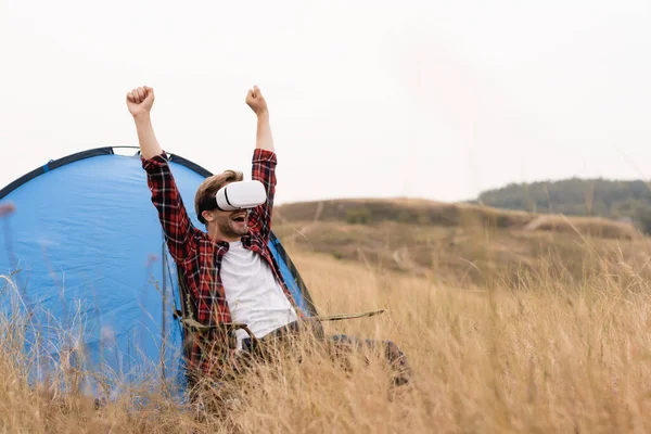 Positive man in virtual reality headset showing yes gesture near tent on meadow — Stock Photo