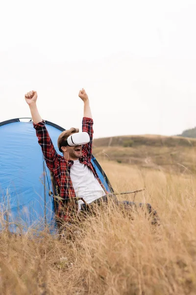 Excited man showing yes gesture while using vr headset near tent during camping — Stock Photo