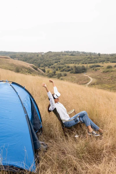 Femme afro-américaine excitée montrant geste ouais tout en utilisant vr casque près de la tente sur prairie — Photo de stock