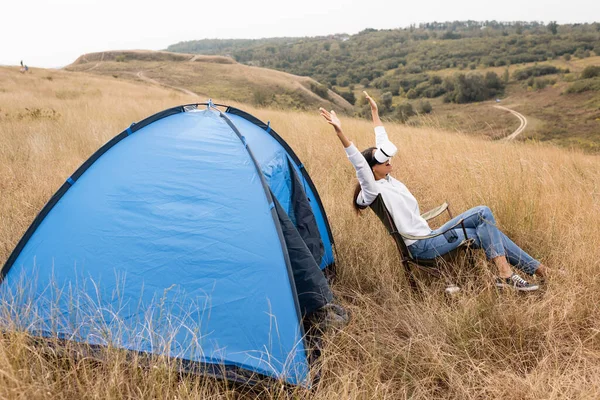 Excited african american woman using virtual reality headset on chair near tent — Stock Photo