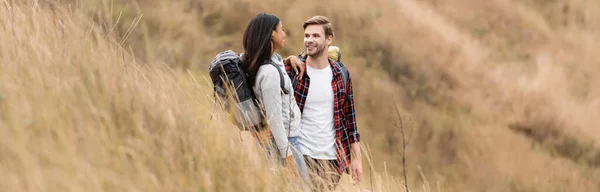 Multiethnic travelers with backpacks looking at each other on hill during trip, banner — Stock Photo