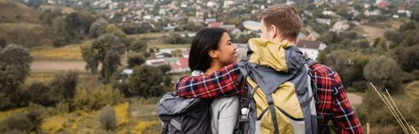 Rückenansicht eines Mannes mit Rucksack, der seine afrikanisch-amerikanische Freundin während der Reise umarmt, Banner — Stockfoto