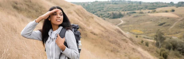 Smiling african american hiker looking away while standing on hill during trip, banner — Stock Photo