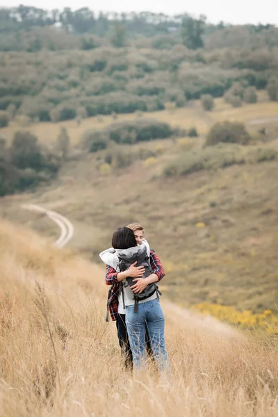 Young man hugging girlfriend with backpack during trip on hill — Stock Photo