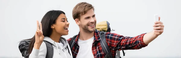 Viaggiatori multietnici sorridenti che parlano selfie con smartphone su sfondo grigio, banner — Foto stock