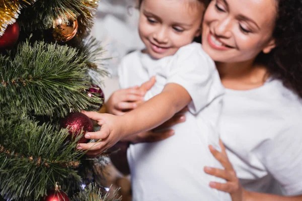 Selektiver Fokus von Mutter und Tochter, die Weihnachtskugel auf festlicher Kiefer berühren — Stockfoto