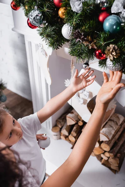 Vista aérea de la madre y la hija tocando bolas de Navidad en ramas de pino - foto de stock