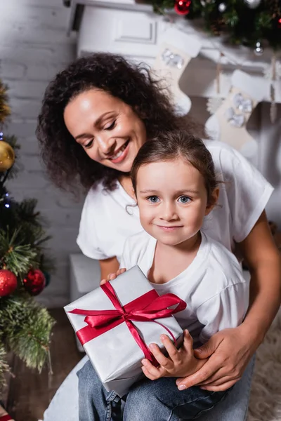 Madre abbracciando figlia con scatola regalo vicino pino a casa — Foto stock