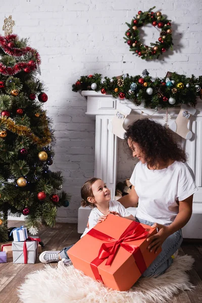 Mother and daughter looking at each other near big gift box at home — Stock Photo