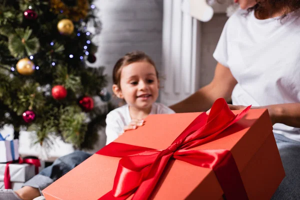 Focus selettivo della grande confezione regalo con nastro rosso vicino a madre e figlia — Foto stock