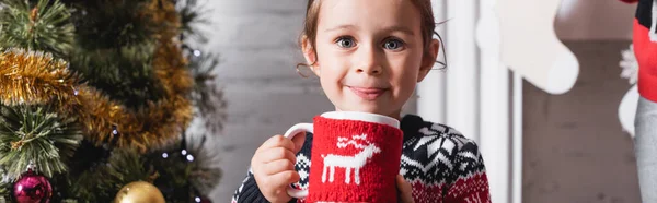 Panoramic shot of girl holding cup with knitted holder and looking at camera — Stock Photo