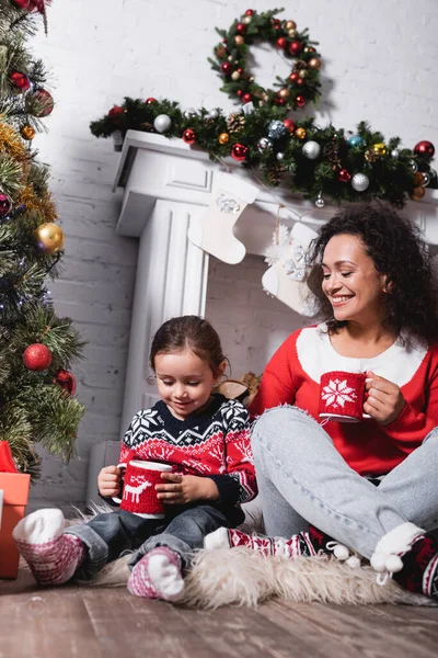 Low angle view of mother and daughter sitting on rug near pine at home — Stock Photo