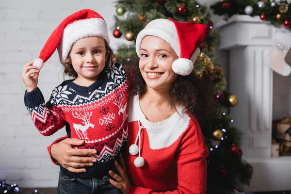 Selective focus of mother and daughter embracing and looking at camera at home — Stock Photo