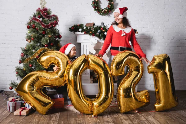 Fille et mère dans des chapeaux de Père Noël debout derrière des ballons avec des numéros — Photo de stock