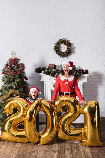 Excited mother and daughter standing near balloons with numbers near pine — Stock Photo