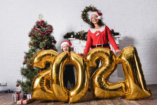 Daughter and mother in santa hats standing near balloons with numbers — Stock Photo