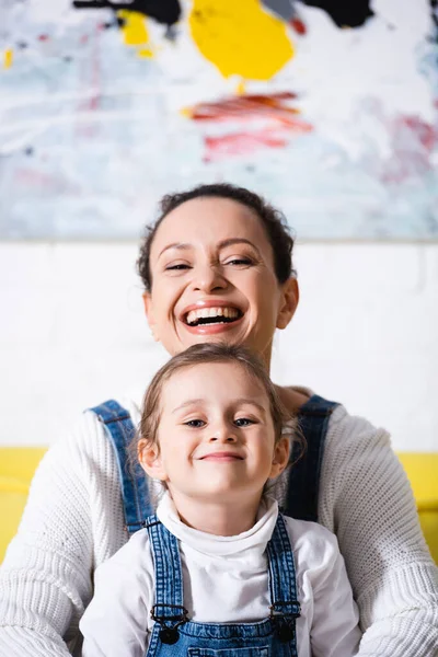 Enfoque selectivo de mamá y su hija mirando a la cámara con la imagen en el fondo - foto de stock