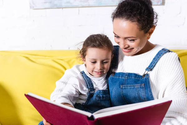 Мати обіймає доньку читати книгу вдома — стокове фото