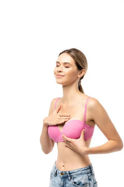 Jeune femme aux yeux fermés touchant le sein en soutien-gorge rose isolé sur blanc — Photo de stock