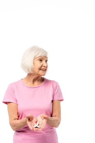 Donna anziana che tiene il nastro rosa della consapevolezza del cancro al seno e distogliendo lo sguardo isolato sul bianco — Foto stock